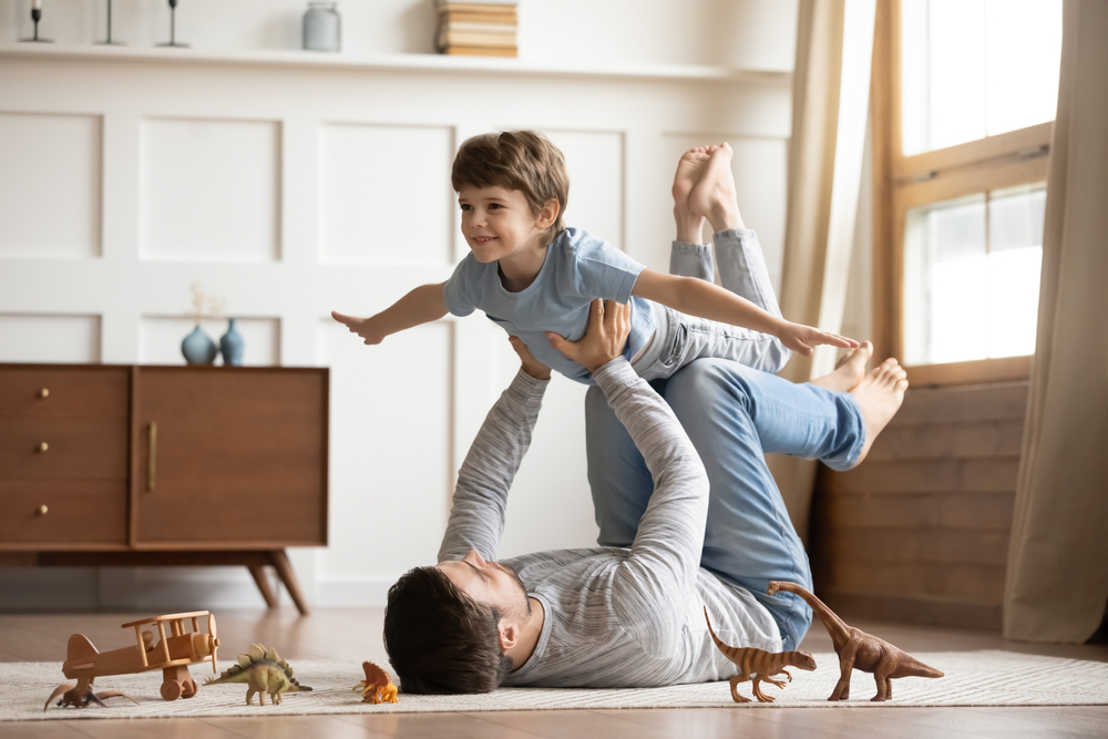 Joyful father on a chic carpet, lifting his excited son in their New Orleans home, illustrating a fun family moment in a stylish yet practical living room.